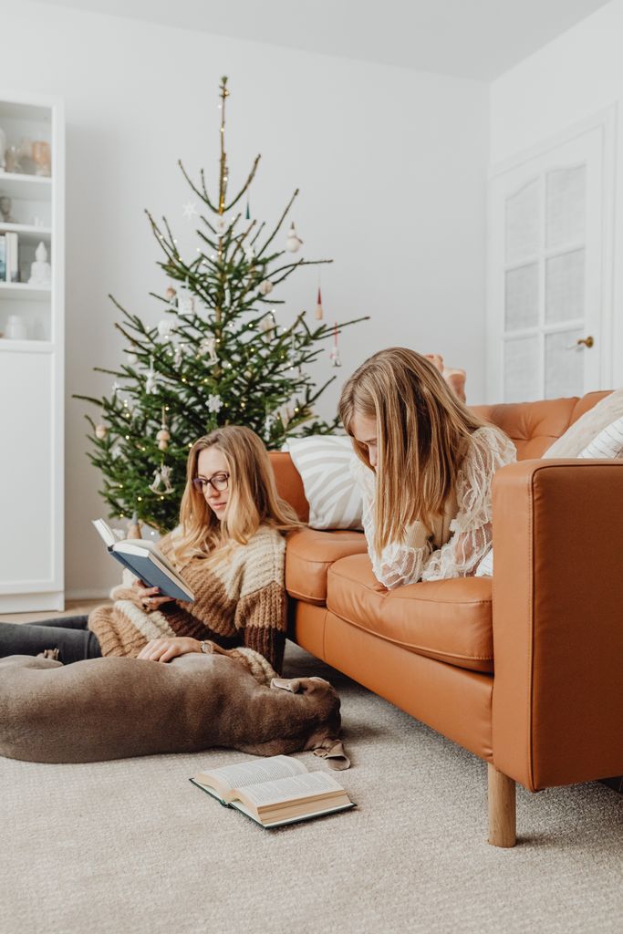 Mother and daughter reading with their dog by the Christmas tree in a cozy living room enscapsulating christmas hygge.