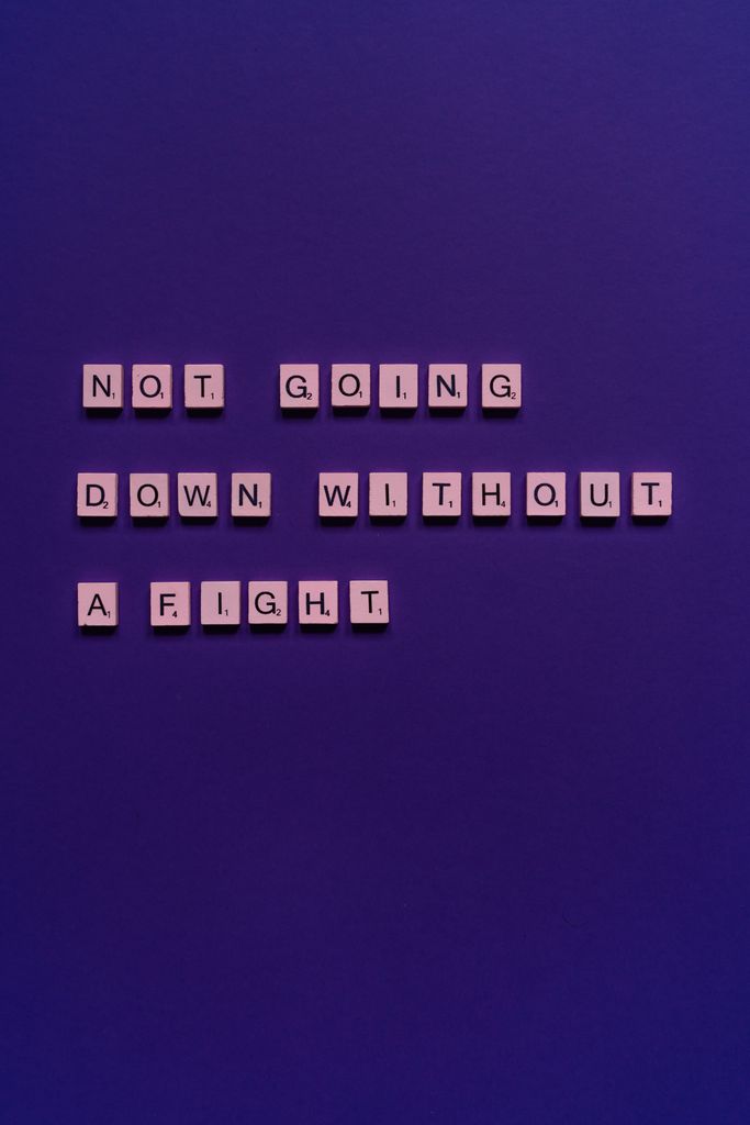 Motivational phrase 'Not going down without a fight' on a purple backdrop using Scrabble tiles.self confidence affirmations
