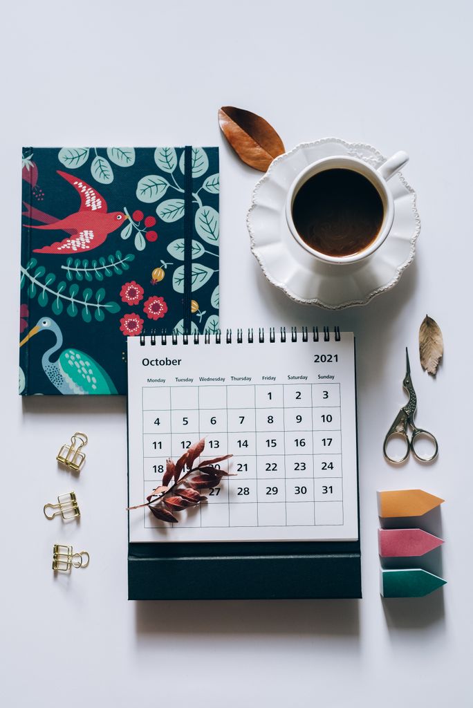 October-themed flat lay with calendar, coffee, notebook, and stationery on white background. monthly goals journal