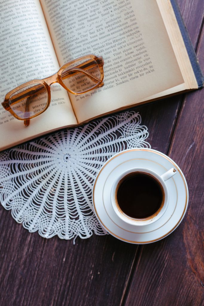 Open book with glasses and coffee on a wooden table, cozy home setting.