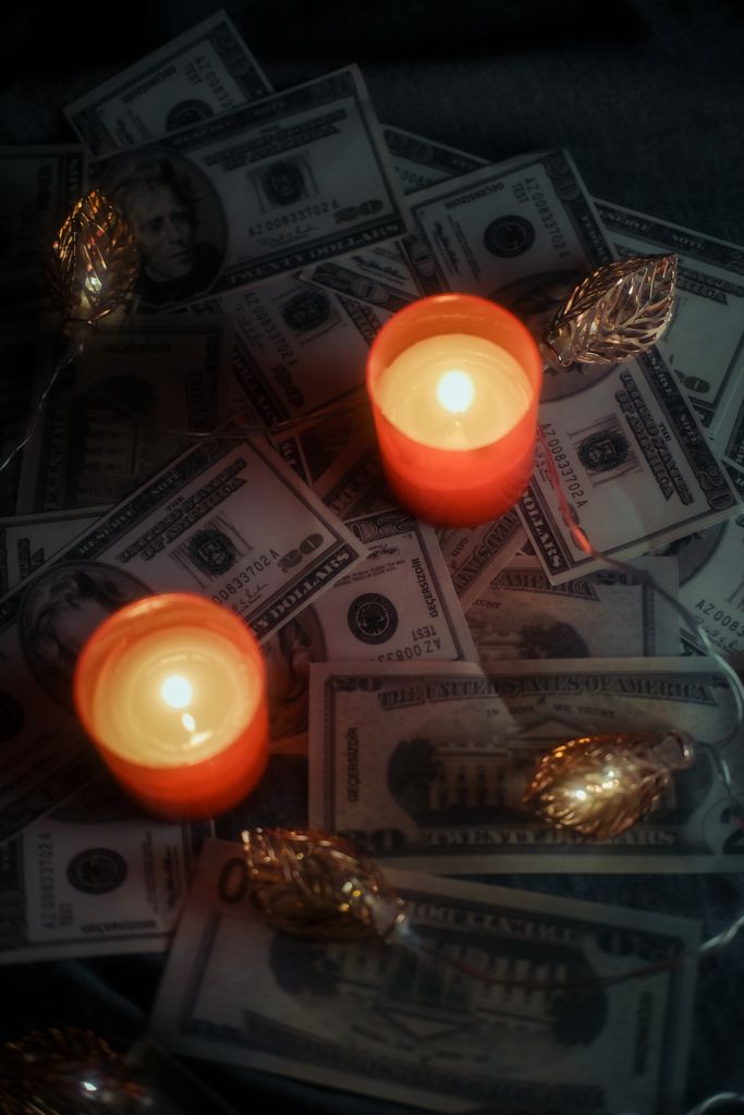 Orange candles glowing on a pile of US dollar bills, symbolizing wealth and expenditure.