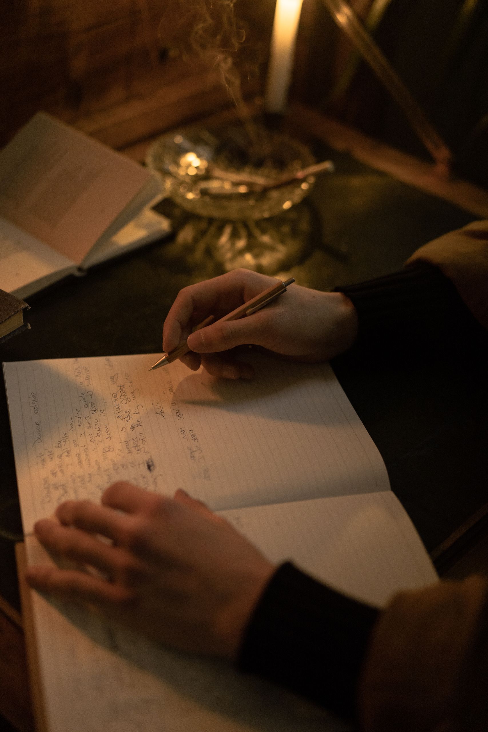 Person writing in a notebook by candlelight, creating a warm, nostalgic ambiance.