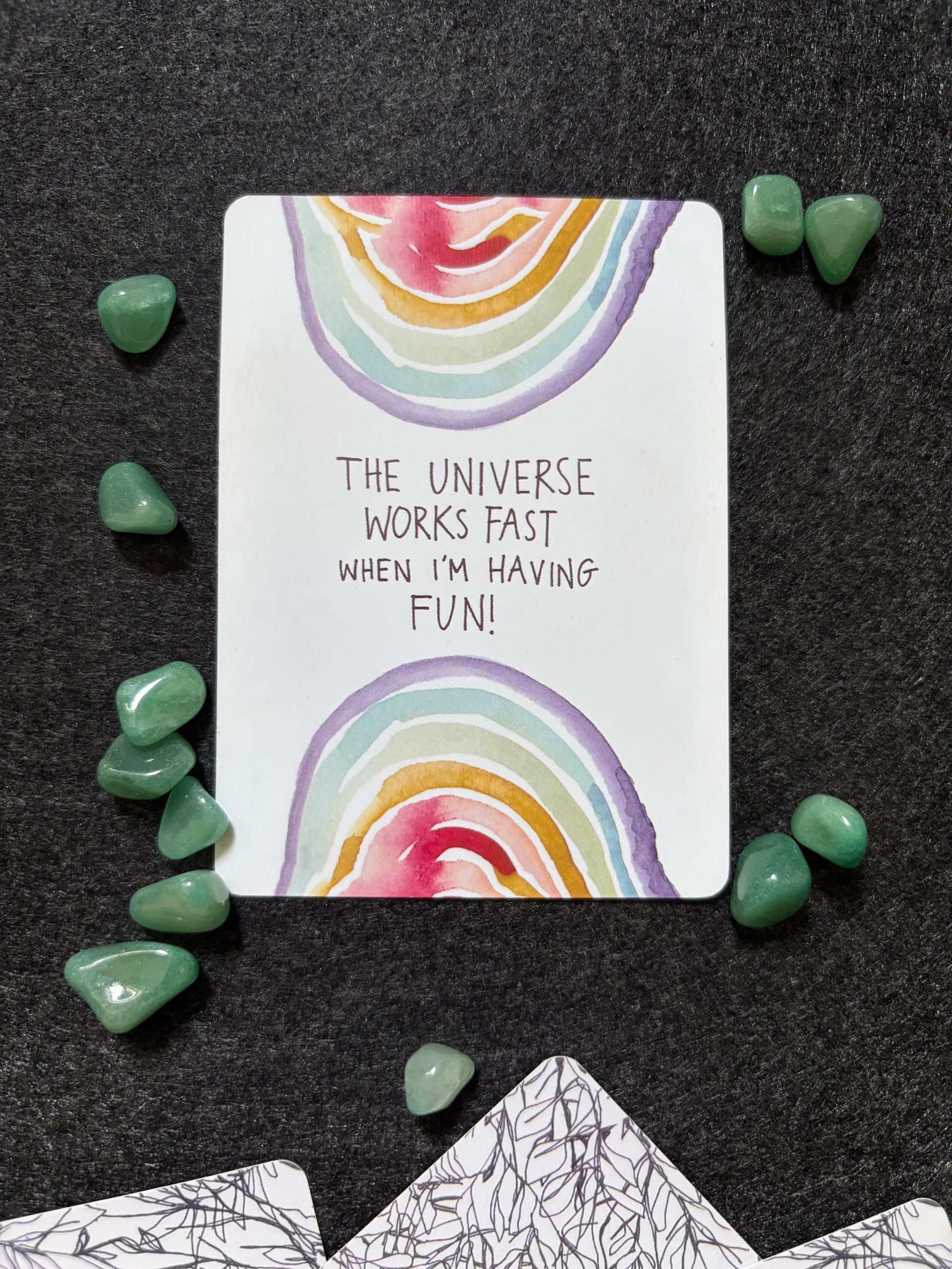 Rainbow-themed motivational card surrounded by green crystals for positive energy.