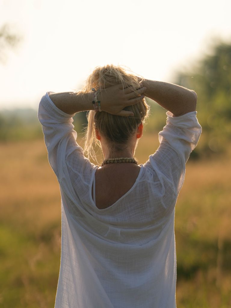 Rear view of a woman in a white shirt with hands up, enjoying a sunny day outdoors.reset nervous system