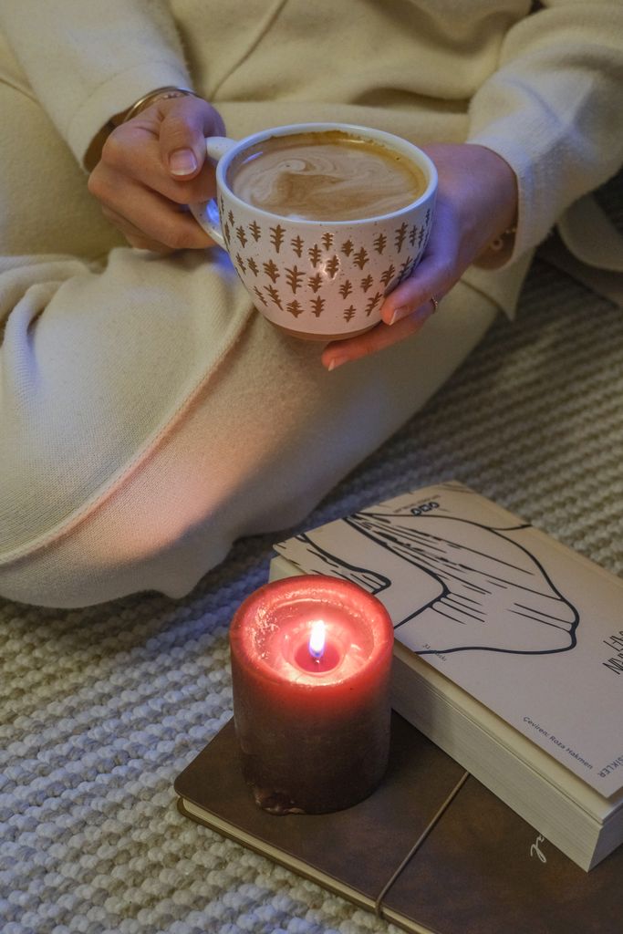 Relaxing scene with a person enjoying coffee, candlelight, and a book indoors.