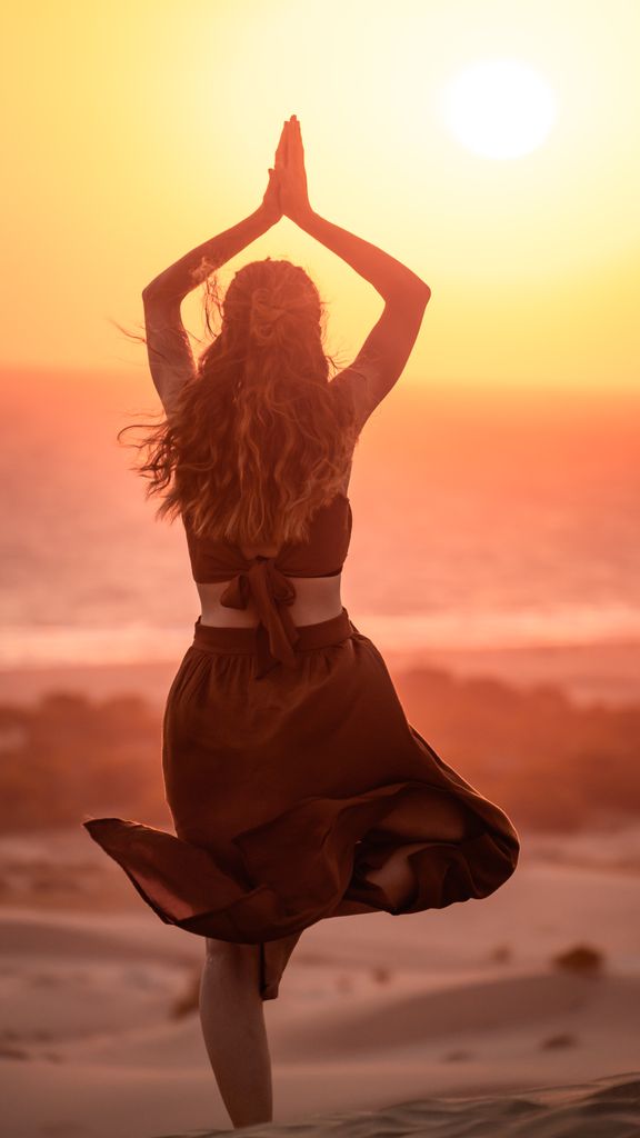 Serene scene of a woman performing yoga during sunset on Antalya's beach with a warm glow.