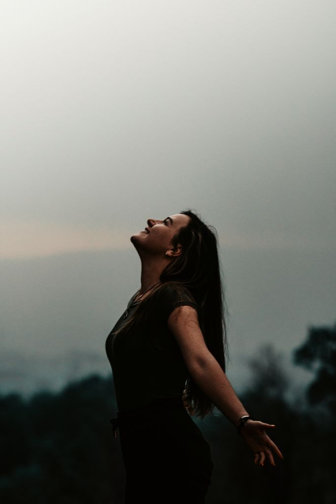 Side view of a woman with arms outstretched, embracing freedom against a misty evening backdrop.