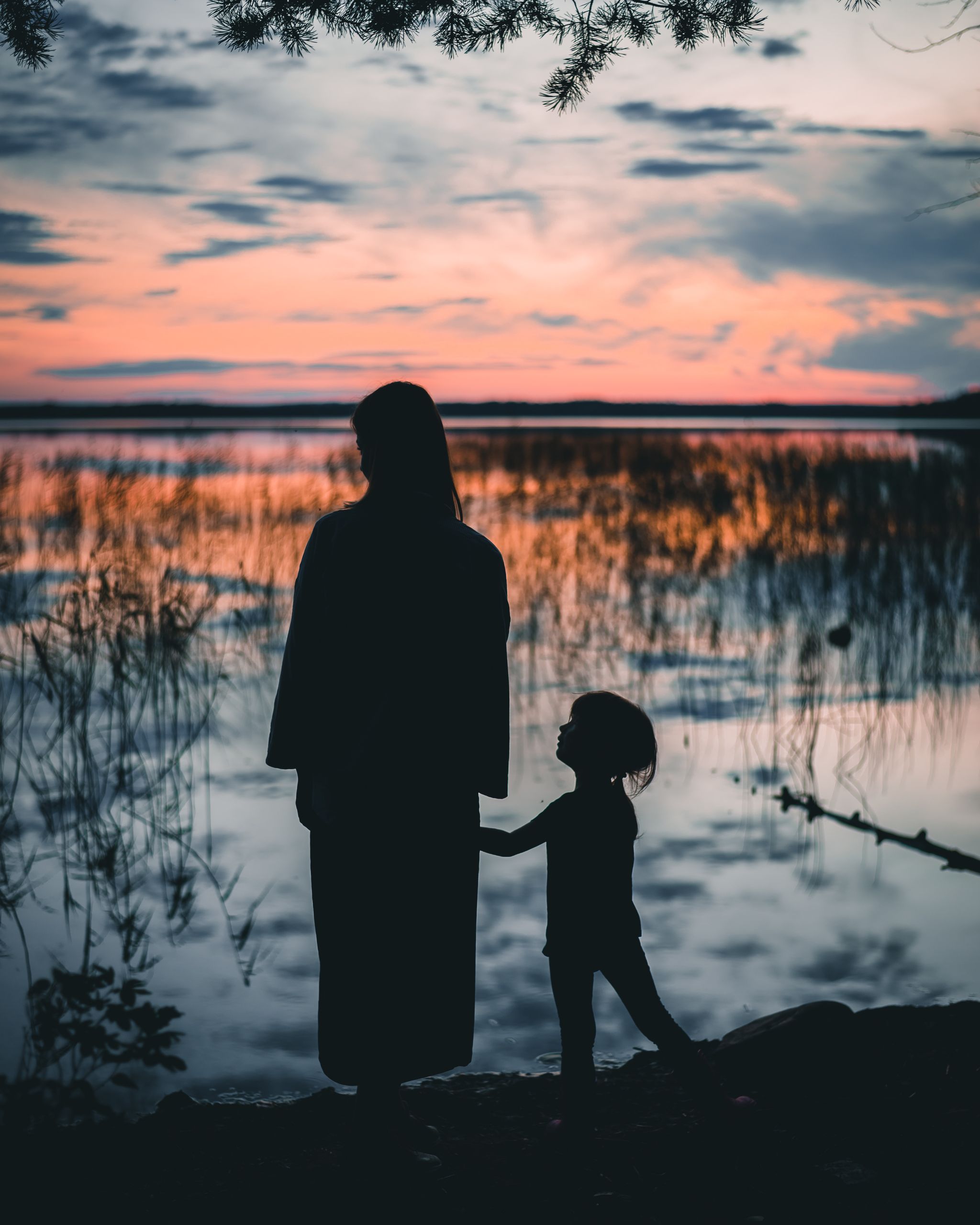 Silhouette of a mother and child by a serene lake at sunset, capturing a tender family moment.