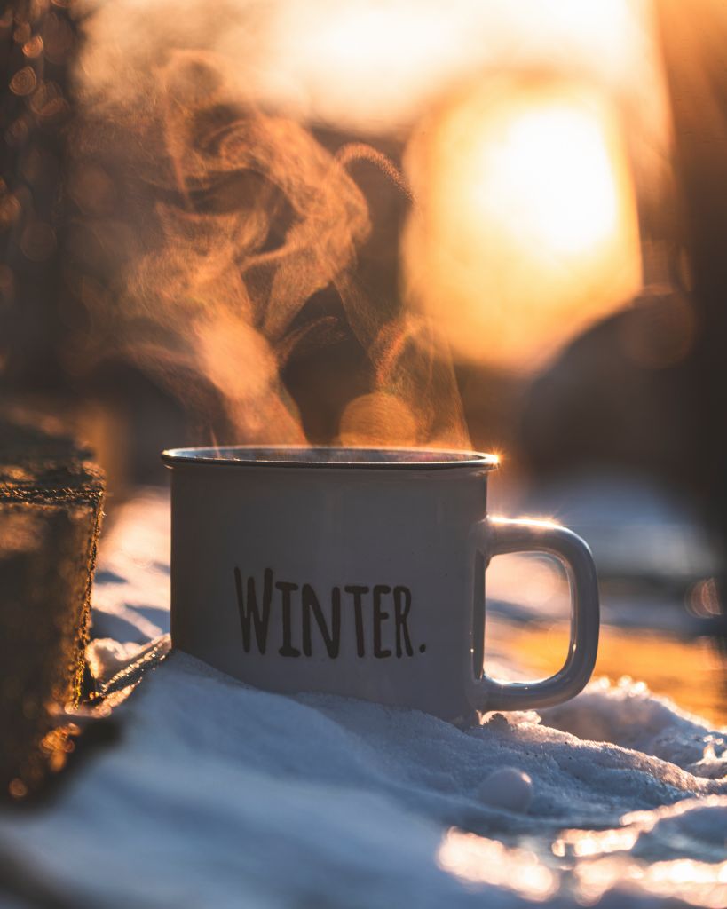 Steaming coffee mug labeled 'Winter' against a glowing sunset, perfect for chilly days.