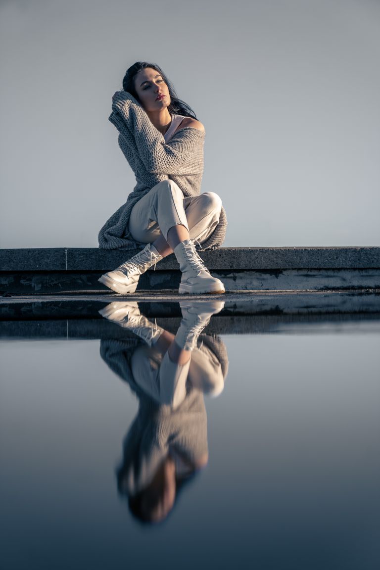 Stylish woman in cozy attire reflects by a puddle, Dublin outdoors.