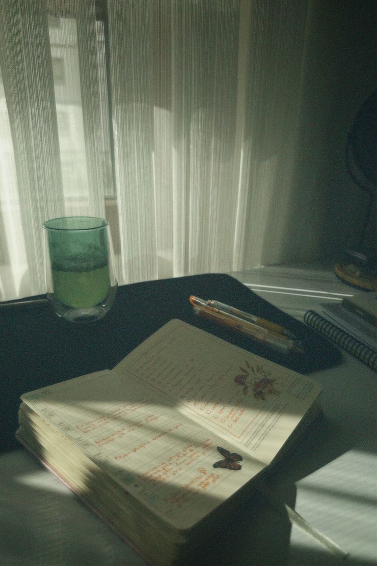 Sunlight streams onto an open notebook with a green drink beside it, creating a peaceful work atmosphere.