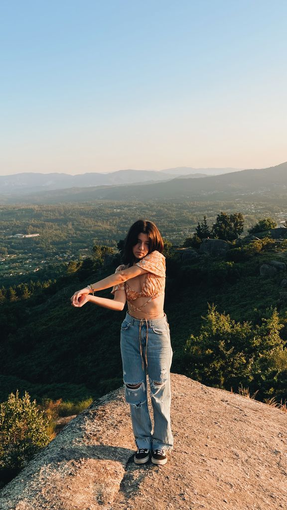 Teenage girl with long hair stretches on a rocky mountain overlook with a beautiful valley view.