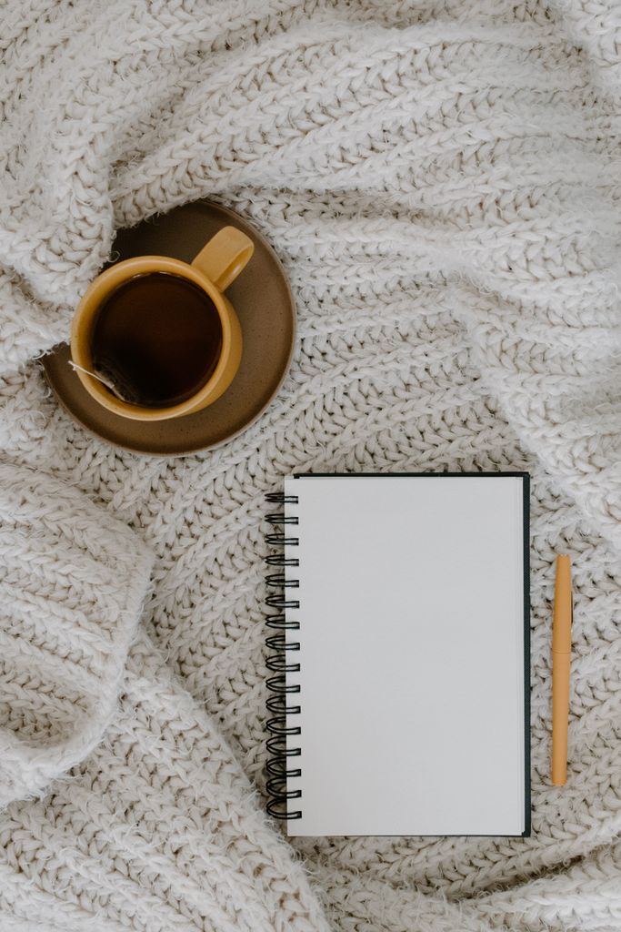 Top view of a cozy scene with a coffee cup, notebook, and knitted blanket, perfect for relaxing moments.