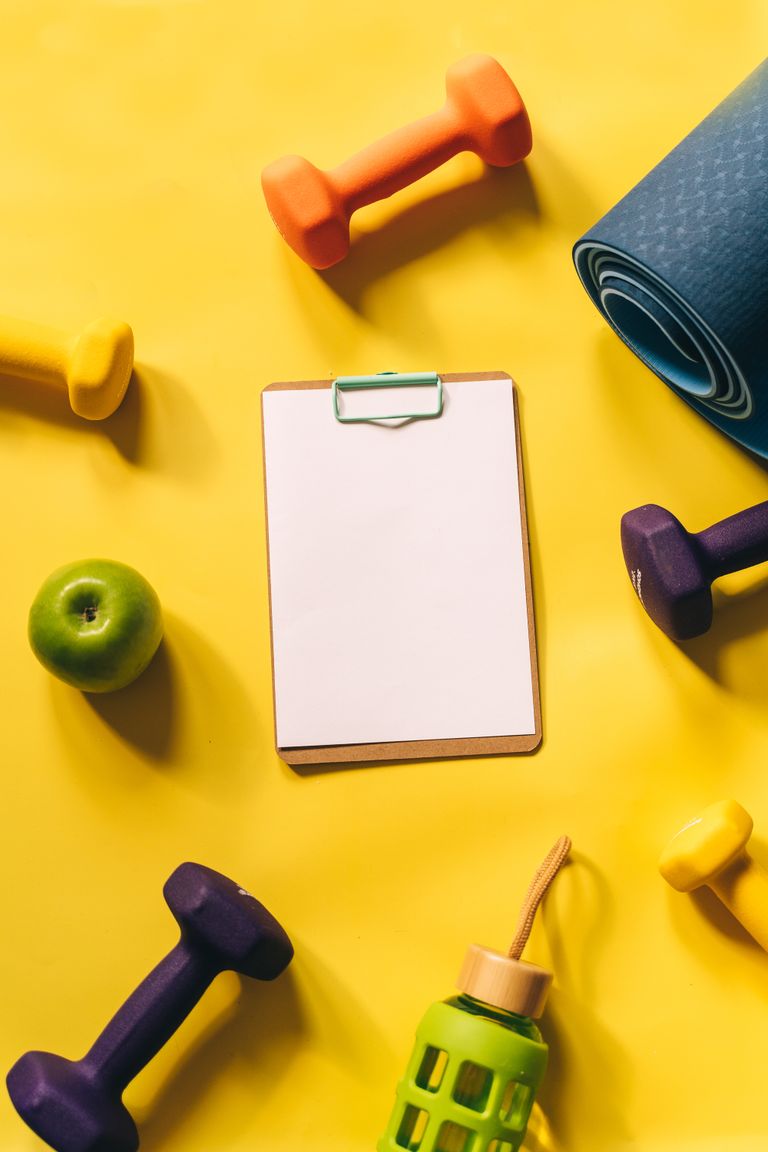 Top view of colorful fitness gear and clipboard on yellow background.