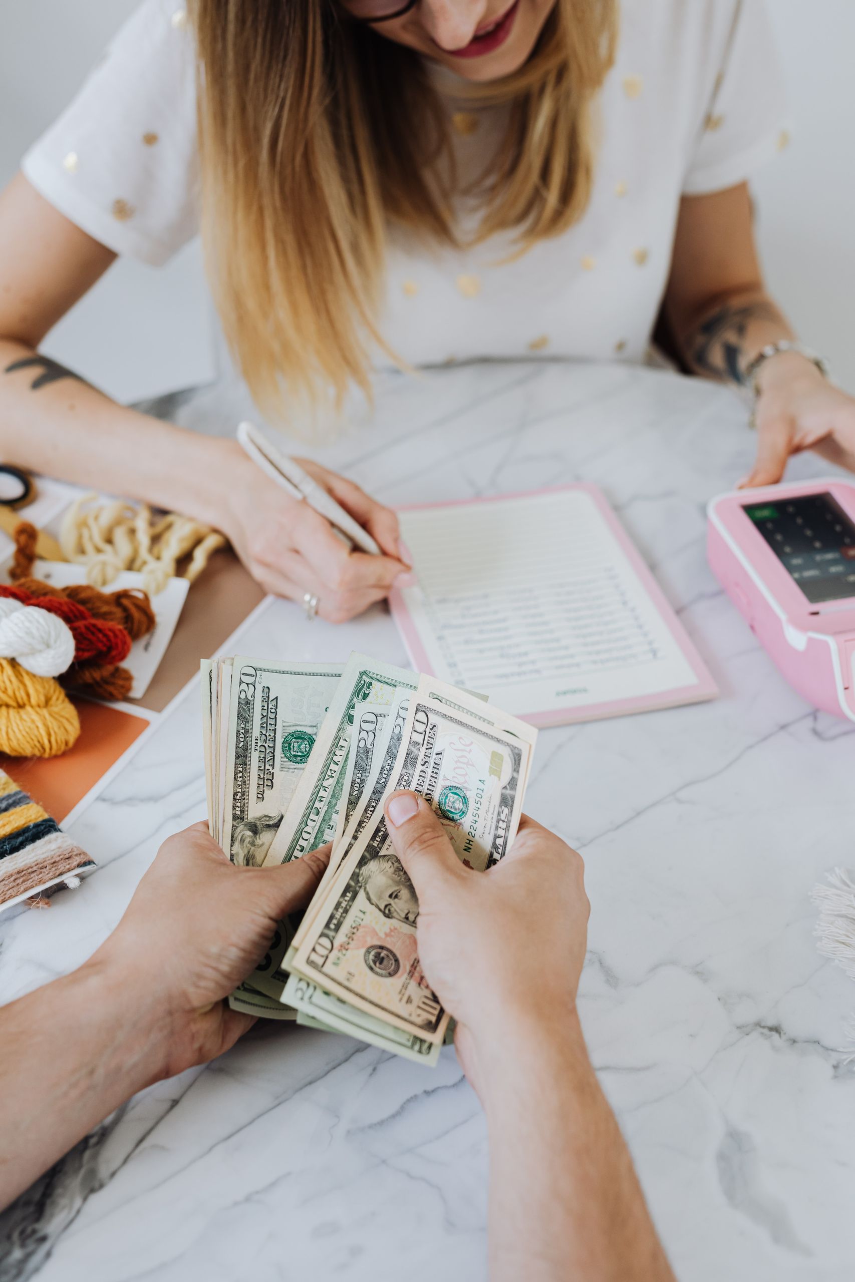 Two adults organizing finances with cash, planner, and card machine indoors.