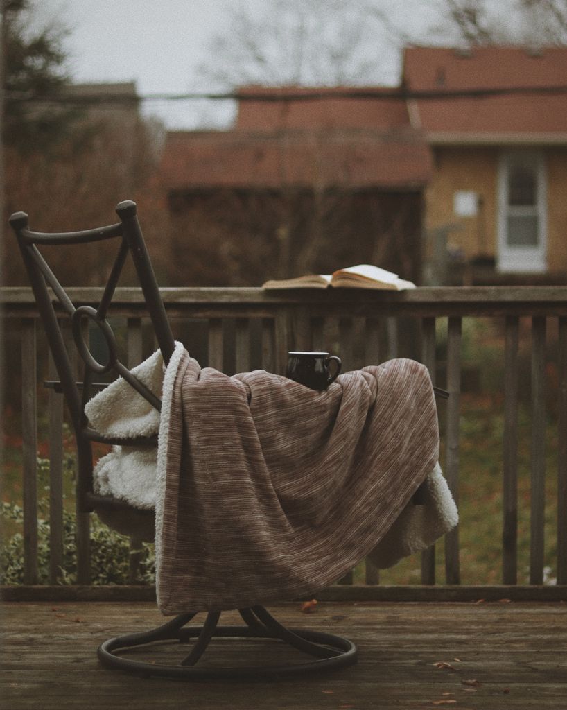 Warm and inviting autumn porch scene with a blanket-covered chair, a book, and a mug.slow living lifestyle