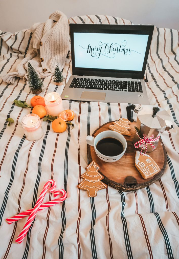 Warm Christmas setting with coffee, laptop, and candles on a bed.