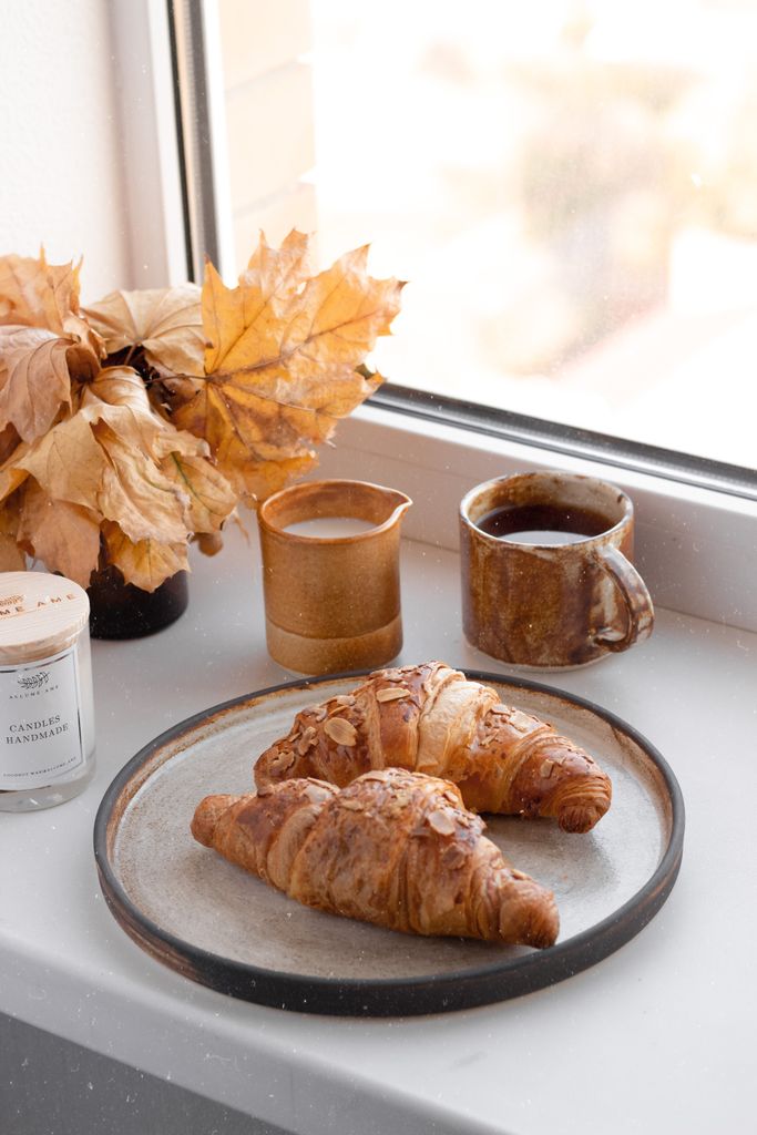 Warm croissants with coffee on a plate by a window, creating an inviting autumn atmosphere.