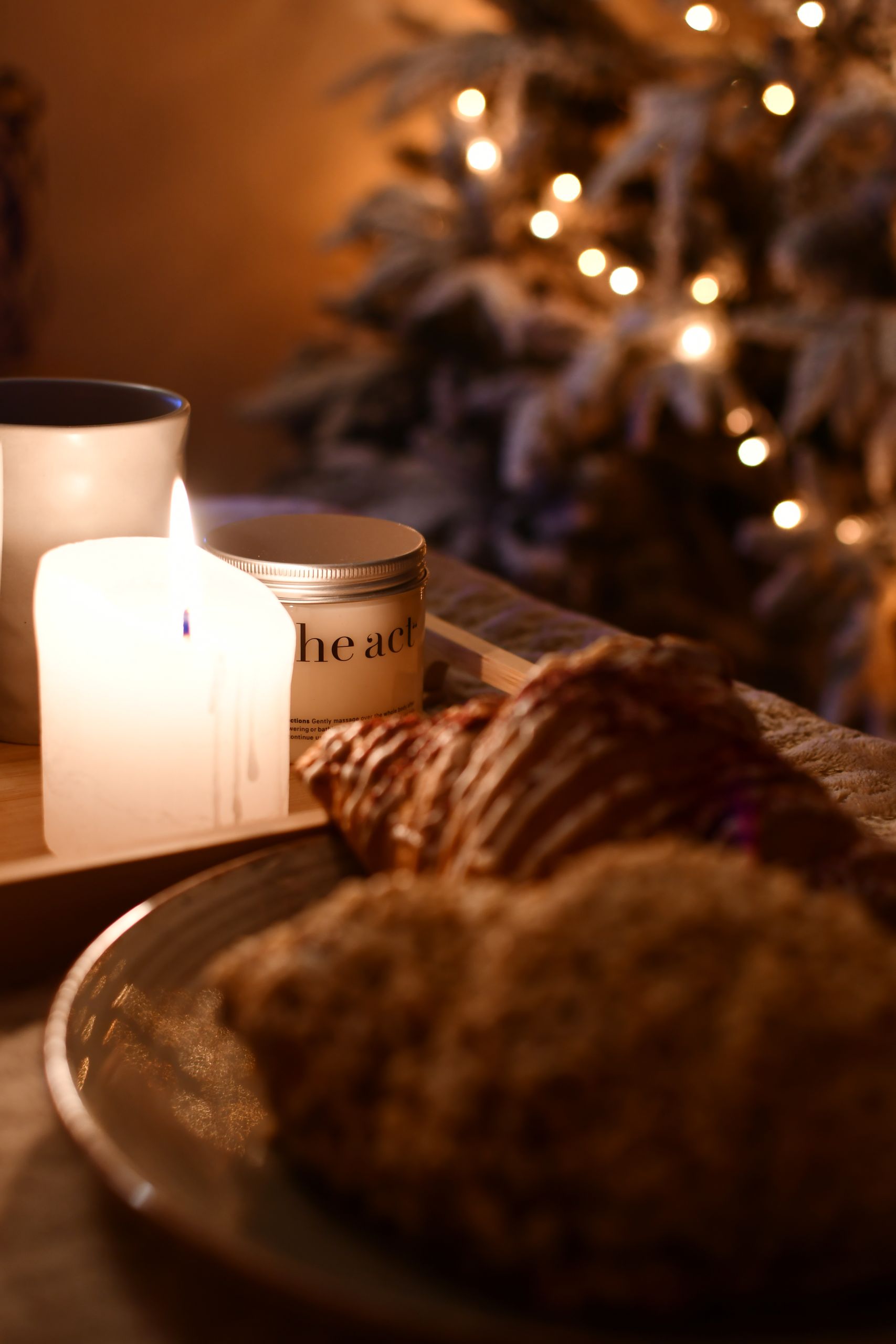 Warm, intimate holiday scene with candle, pastries, and Christmas tree lights.