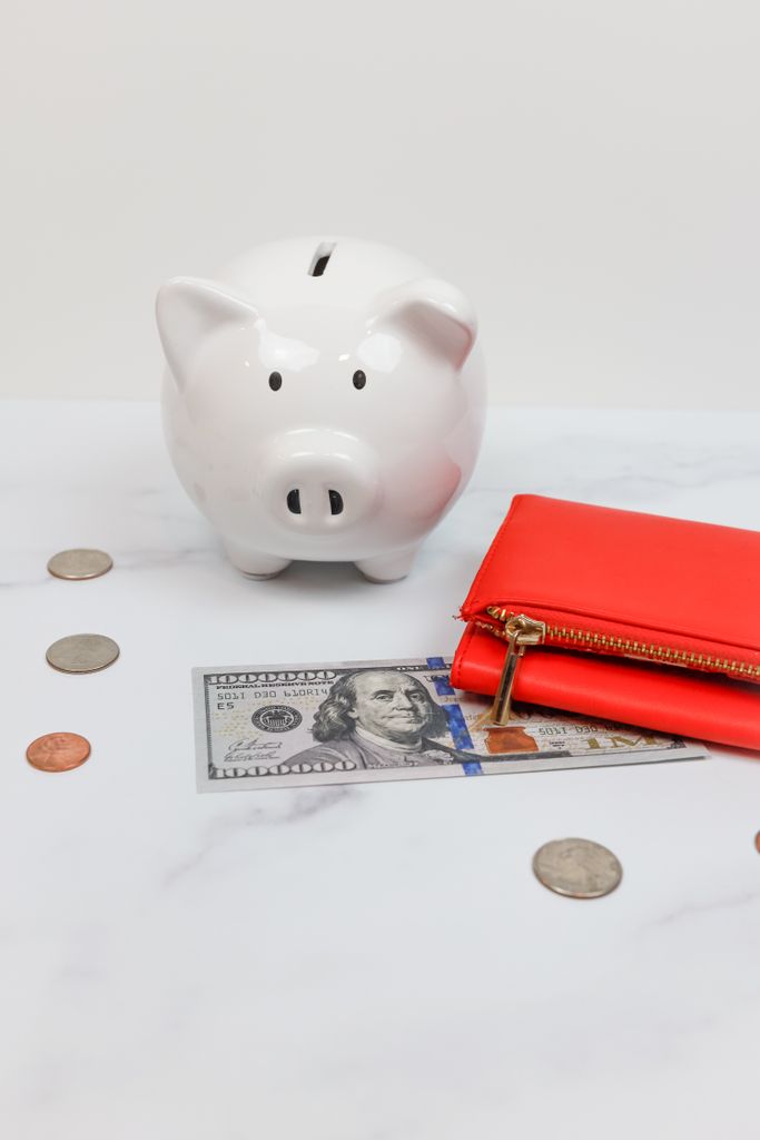 White piggy bank with coins and a red wallet on a marble desk to indicate no spend november