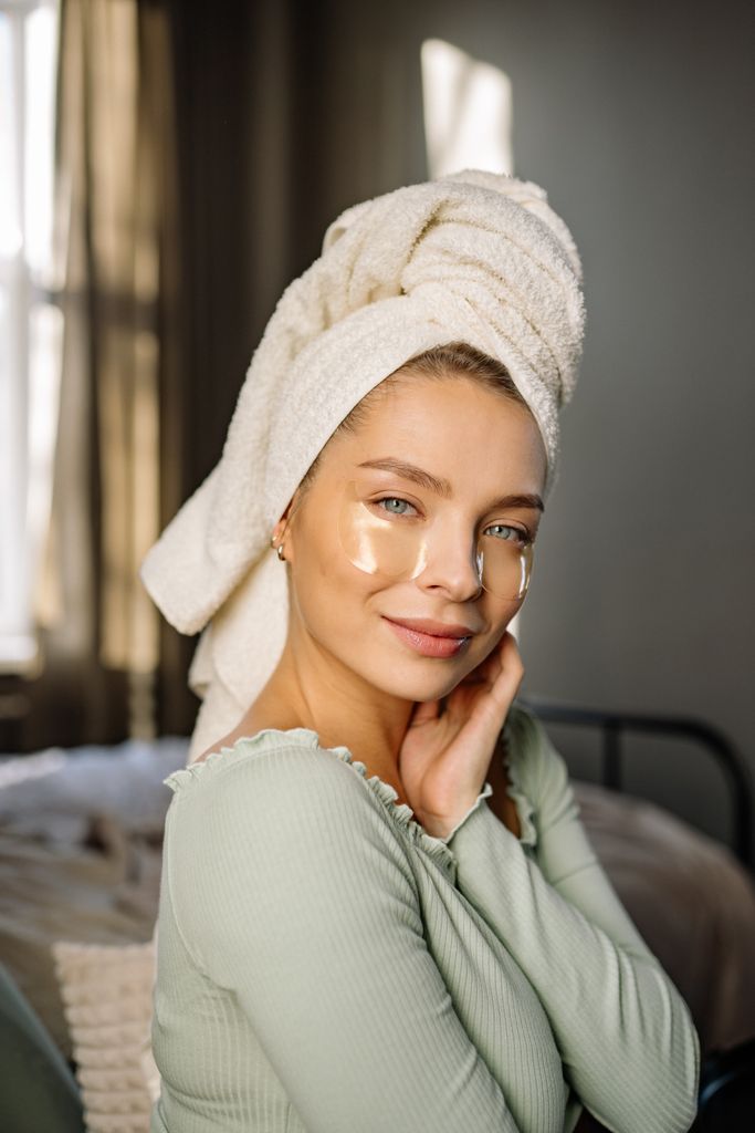 Woman enjoying self-care with eye patches and towel in cozy home setting. new year glow up