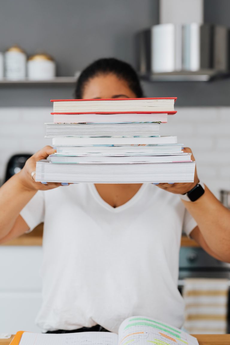 Woman holding a tall stack of various books, symbolizing education and study.