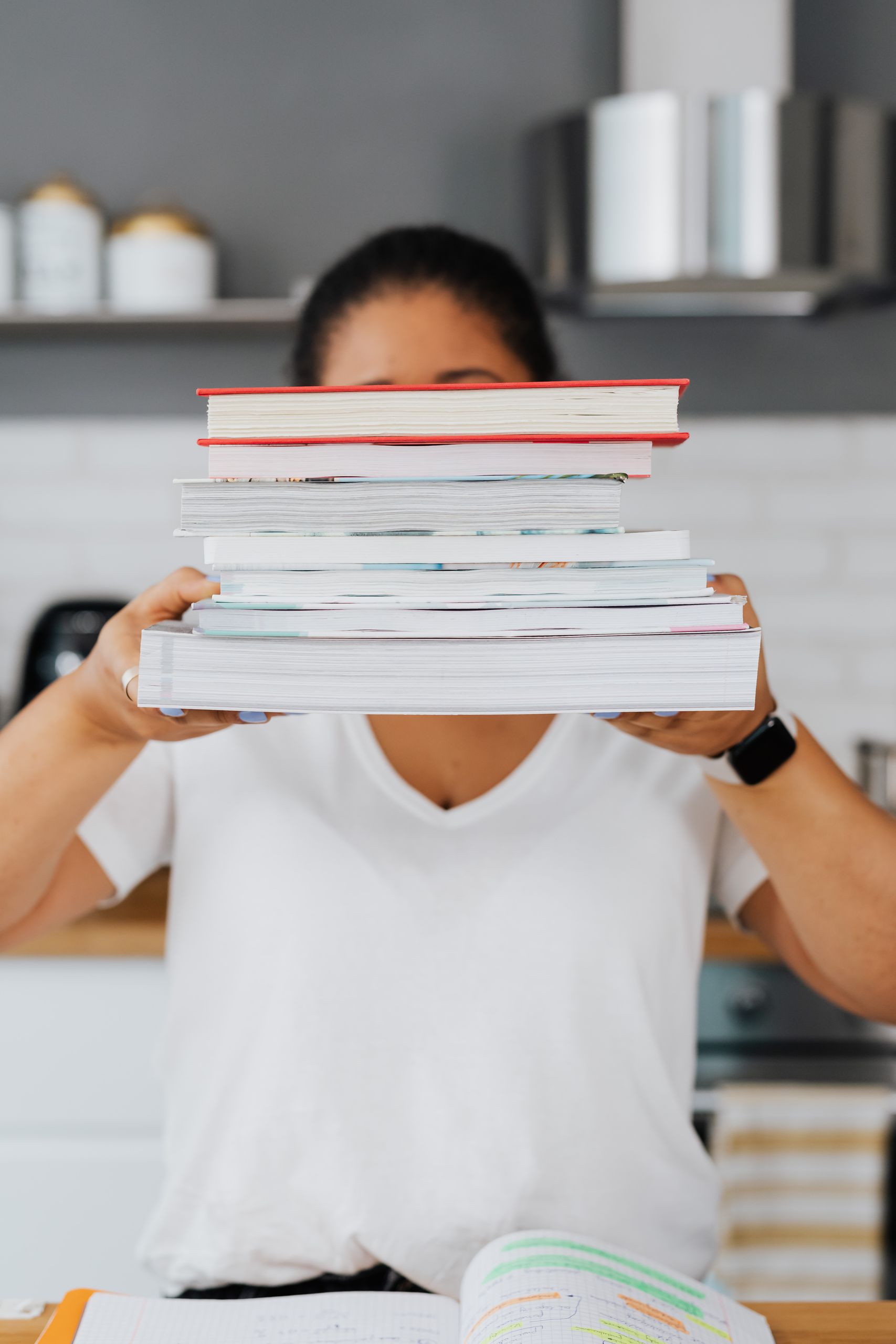 Woman holding a tall stack of various books, symbolizing education and study.