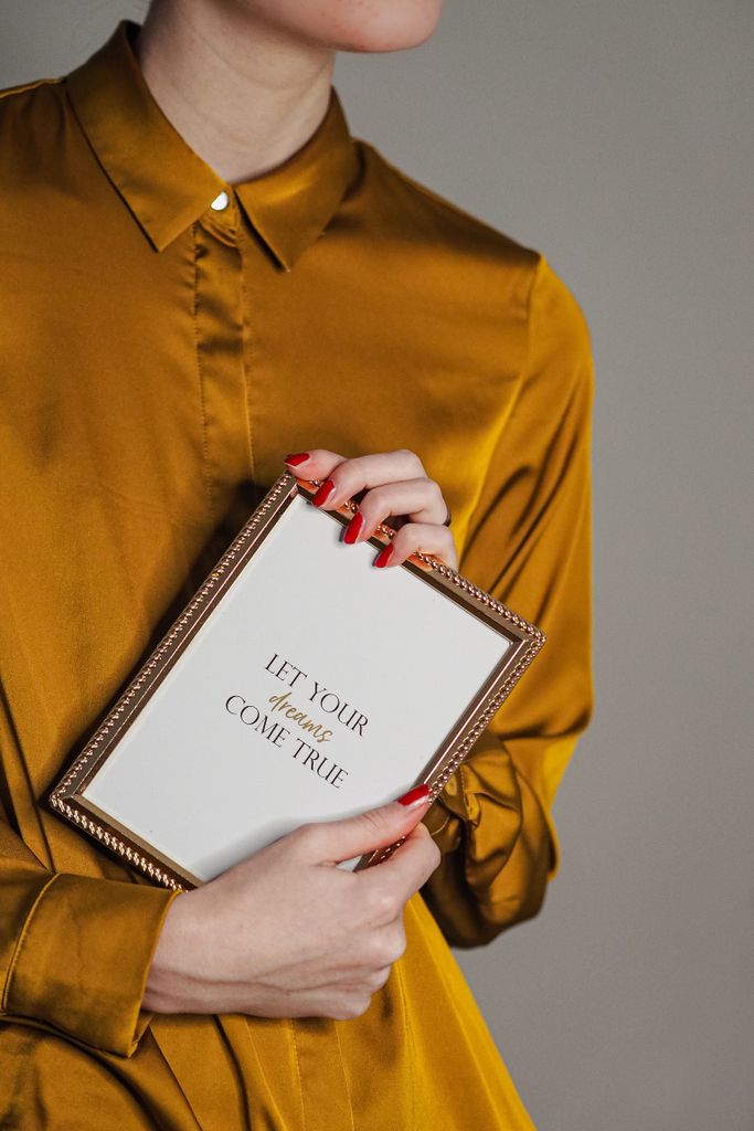Woman in mustard dress holding a frame with inspirational text, closeup.