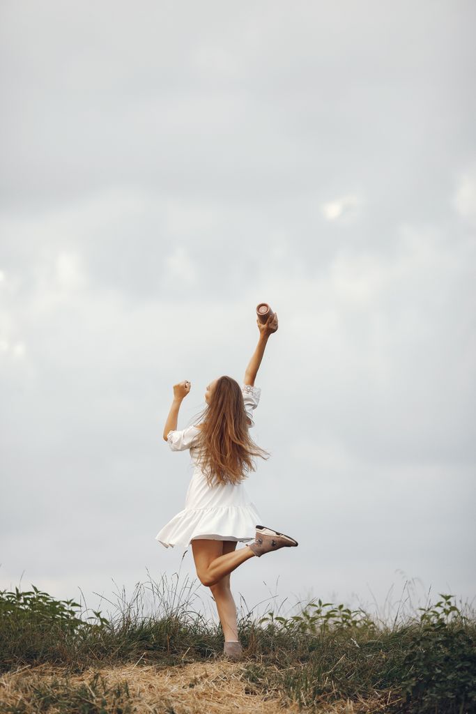 ways to romanticize your life Woman joyfully raising her arms in a white dress amidst nature, symbolizing freedom and happiness.
