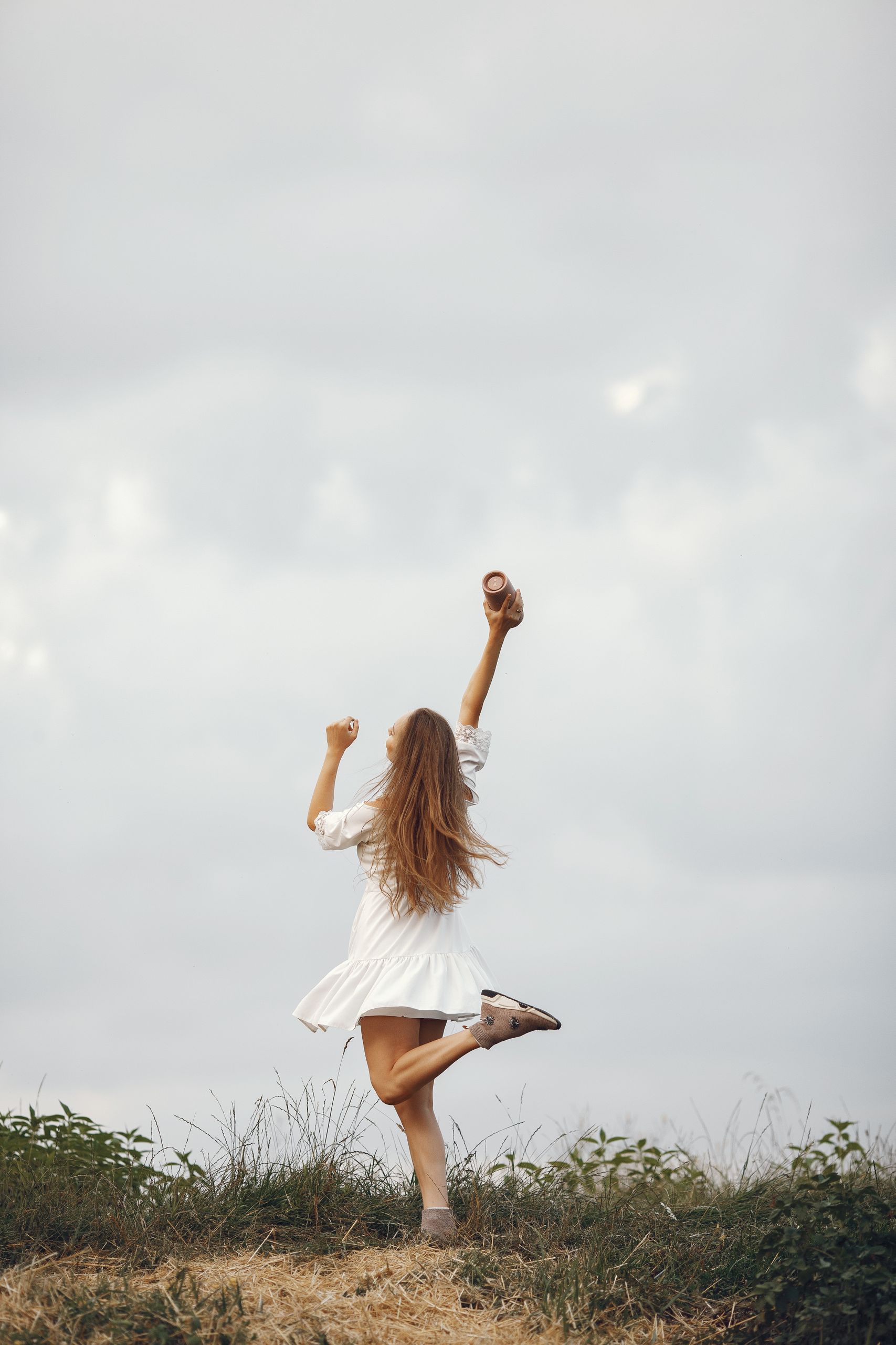Woman joyfully raising her arms in a white dress amidst nature, symbolizing freedom and happiness.