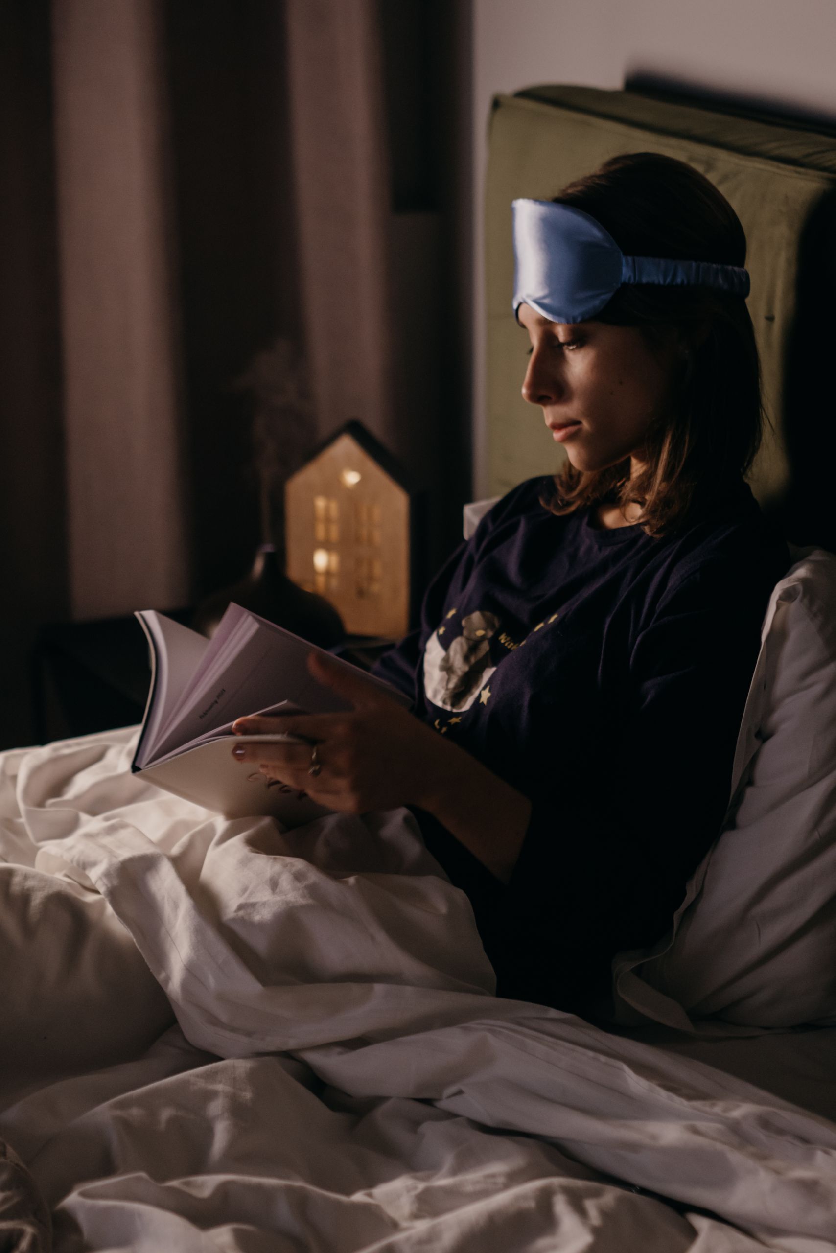Woman reading in bed with a sleep mask, enjoying a cozy and comfortable evening.