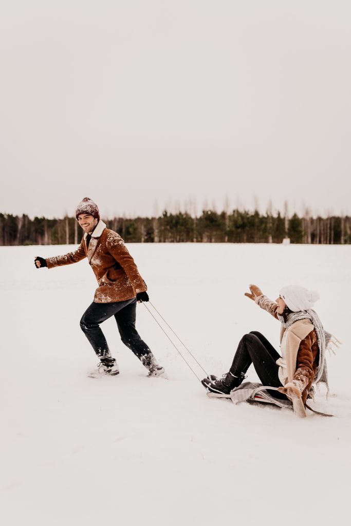 Young couple having fun sledding in a snowy field, wearing warm winter clothing.