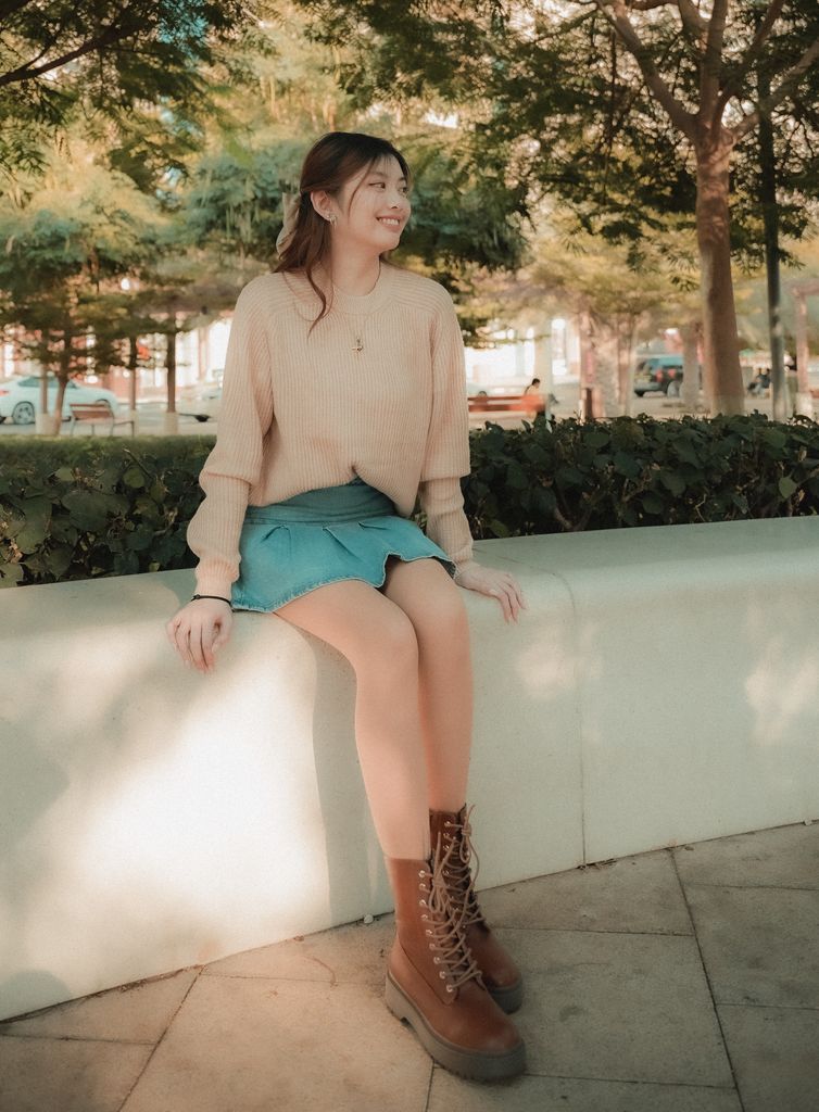 Young woman in a cozy autumn outfit sitting in a park, smiling and enjoying the day. soft life era