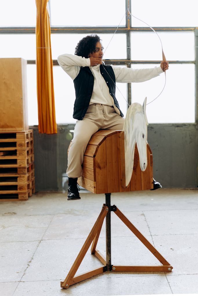 Young woman practicing archery indoors, aiming with concentration and focus.