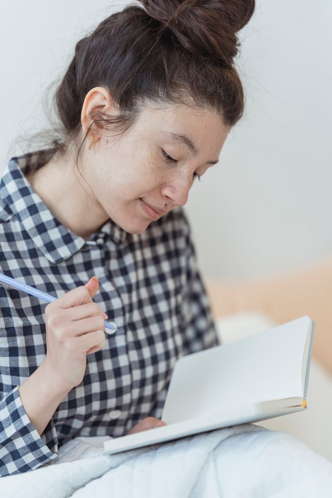 Young woman with pen journaling in a blank notebook, sitting indoors.