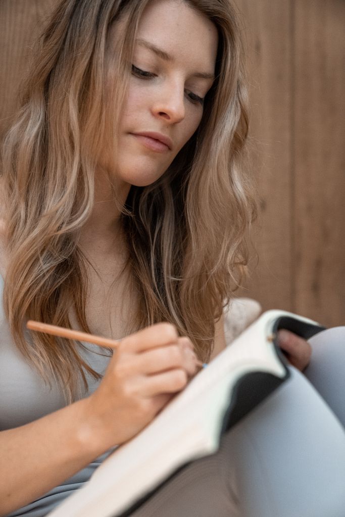 Young woman writing in a notebook indoors. monthly reflection journal prompt